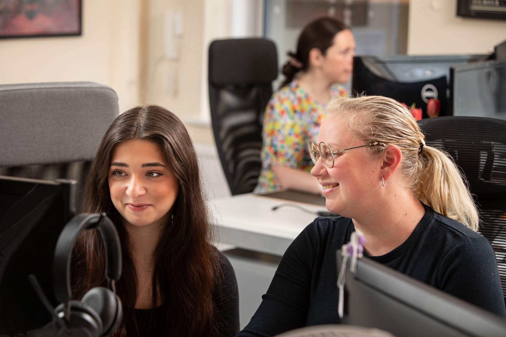 Team members working in croded office, smiling looking at laptop.